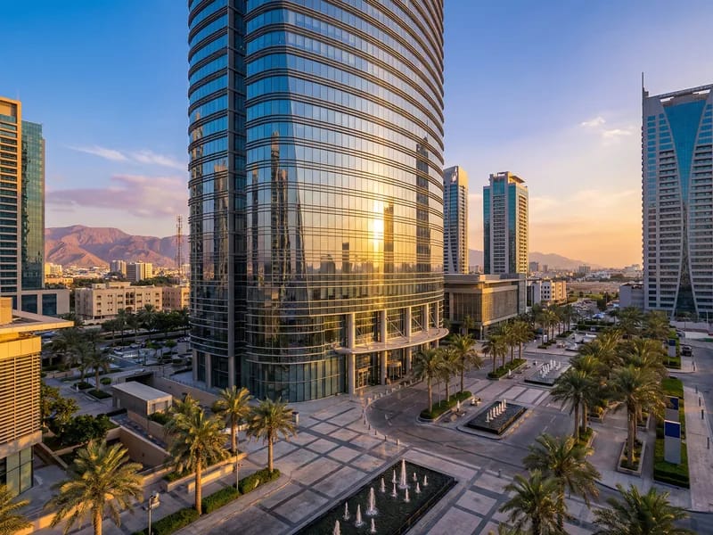 Completed modern glass commercial tower in a Middle Eastern city with palm tree plaza at sunset