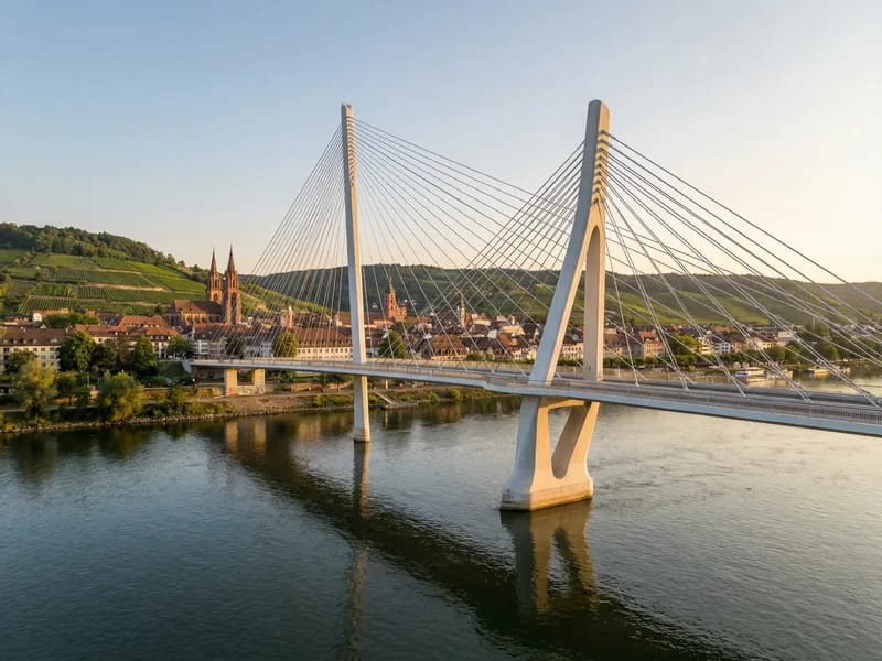 Modern cable-stayed bridge spanning a wide river in a European setting with a historic city in the background